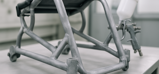Den Sportrollstuhl neu lackieren — was sich vor der neuen Saison lohnt Demontierter Aluminium-Rahmen eines Sportrollstuhls auf einer Werkbank, im Hintergrund eine Lackierpistole